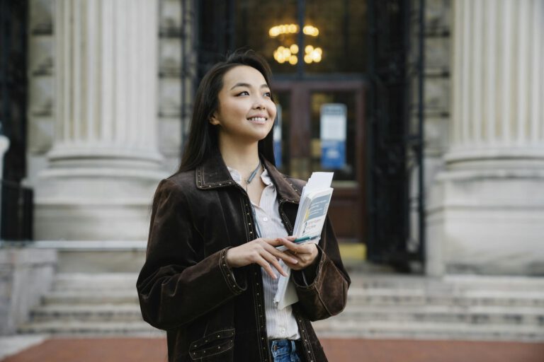 A woman smiles while holding papers outside a historic building, exuding confidence.